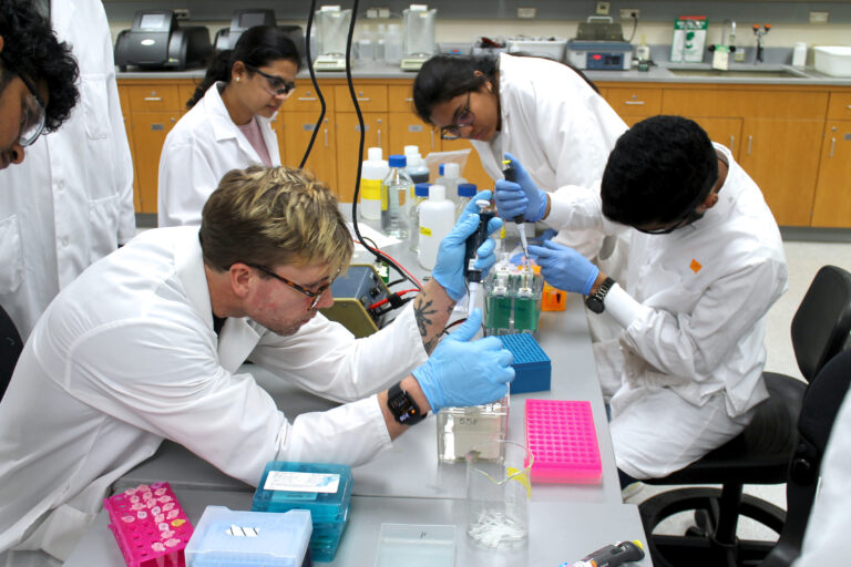An instructor holds up a small plastic tube during a lab for the Applied Drug Development program.